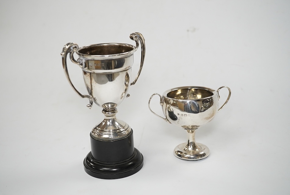 A pair of Edwardian silver dwarf candlesticks, of tapering design, C.S Green & Co, Birmingham, 1908, 13.2cm, together with four small silver trophy cups, a silver napkin ring and a plated trophy cup. Condition - poor to